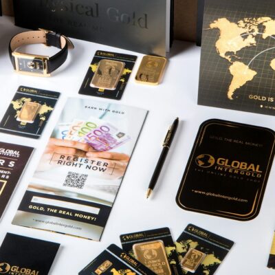 Flat lay of promotional materials for gold investment, featuring brochures, cards, and gold bars.