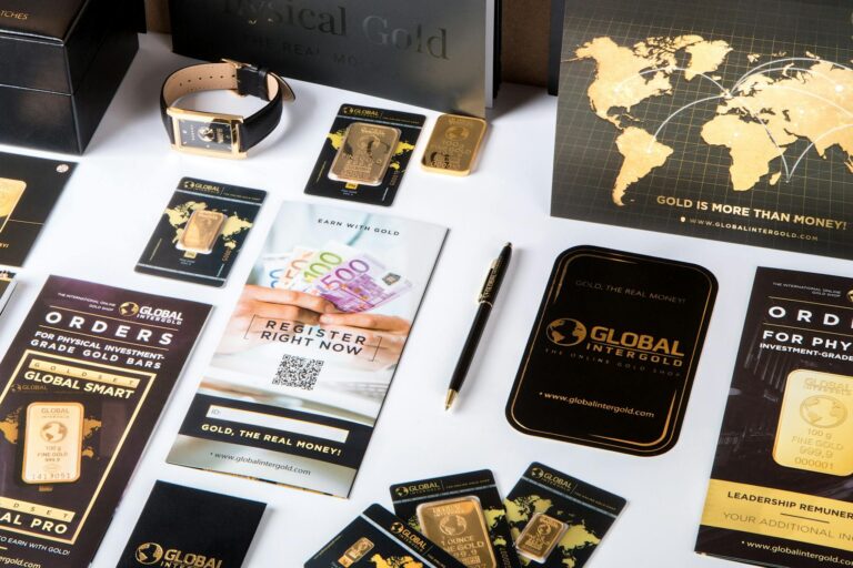 Flat lay of promotional materials for gold investment, featuring brochures, cards, and gold bars.